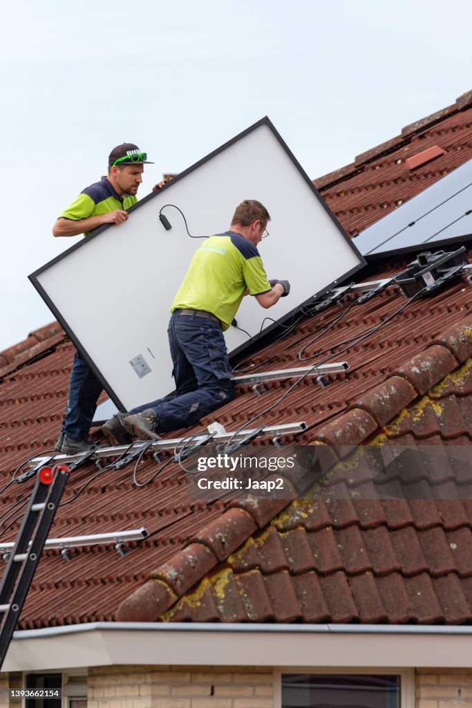 Two men installing solar panels on a tiled roof