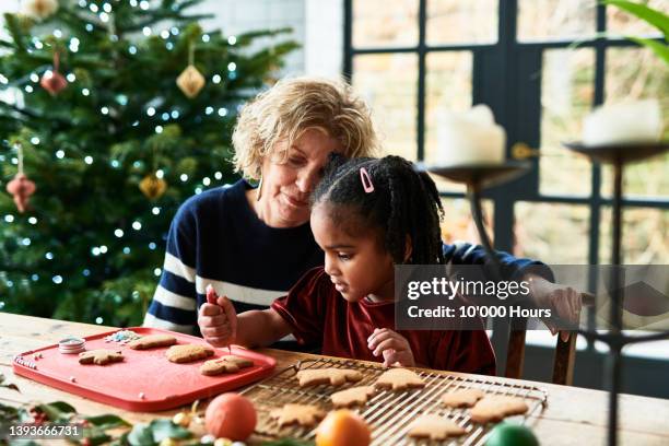 grandmother helping granddaughter decorate christmas cookies - weihnachtskekse stock-fotos und bilder