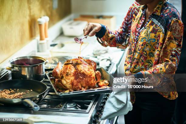 woman basting turkey in roasting tin for christmas dinner - truthahn geflügelfleisch stock-fotos und bilder