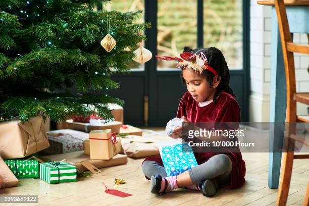 young girl unwrapping christmas present tree - open day 10 stockfoto's en -beelden