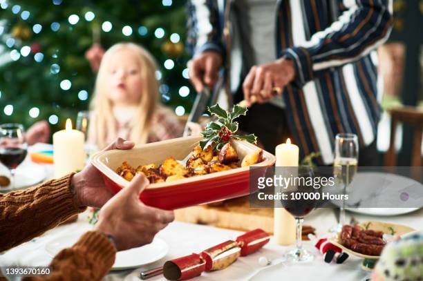 man holding serving dish with roast potatoes and a sprig of holly for christmas dinner - cena fotografías e imágenes de stock