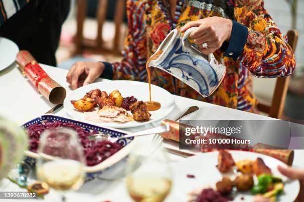 woman pouring gravy onto roast dinner with christmas crackers on table - bratengericht stock-fotos und bilder