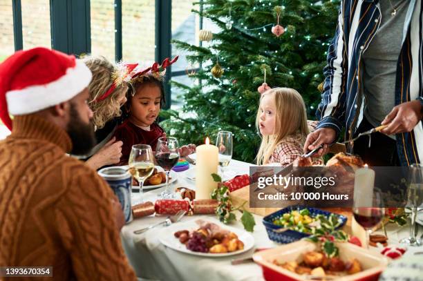 girls sitting at table with family as man carves christmas turkey - roast dinner table stock pictures, royalty-free photos & images