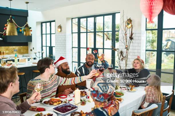cheerful multi ethnic family raising glasses at christmas dinner - holiday dinner stock-fotos und bilder
