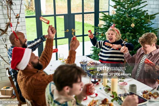 family pulling christmas crackers over christmas dinner - christmas fun stock pictures, royalty-free photos & images