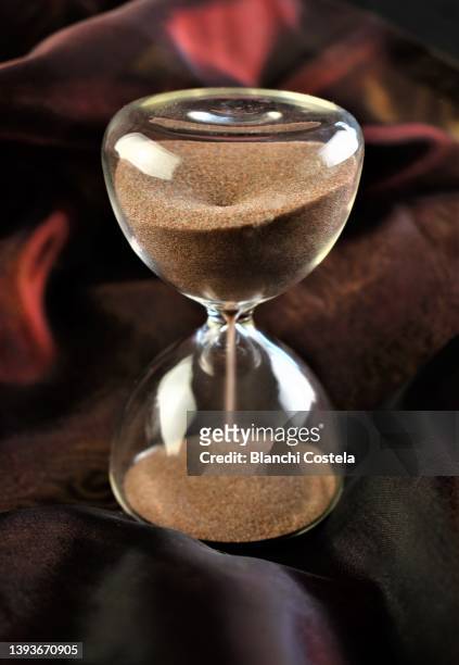 hourglass on brown silk - business dunkler hintergrund studioaufnahme stock-fotos und bilder