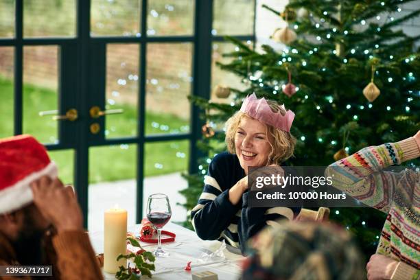 cheerful mature woman wearing christmas cracker hat playing games after dinner and laughing - christmas fun stock pictures, royalty-free photos & images