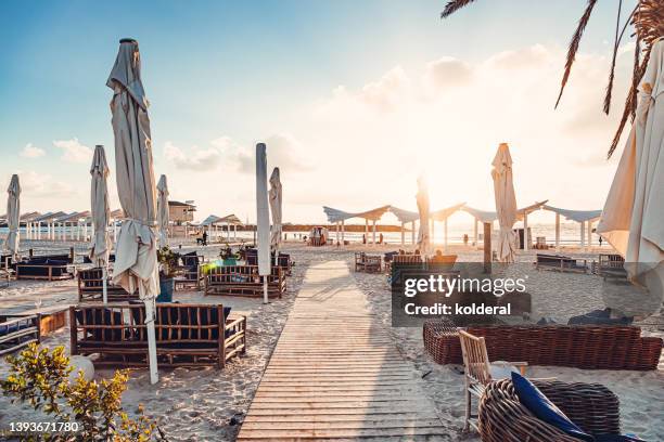 mediterranean beach cafe with wooden deck and lounge sofas on the sand, scenic mediterranean sunset - outdoor lounge stockfoto's en -beelden