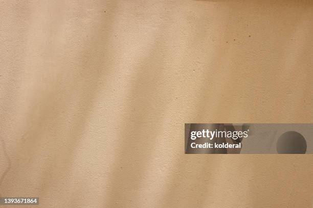 tan colored wall, stucco textured effect in bright sunlight with light trees shadow casted on the wall - yellow wall stock pictures, royalty-free photos & images