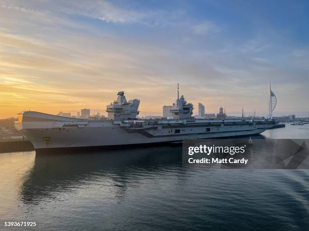 The sun rises behind the Royal Navy's HMS Queen Elizabeth aircraft carrier moored in the Royal Navy Dockyard besides the Spinnaker Tower on April 18,...