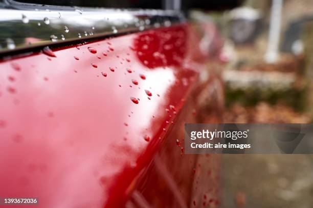 close-up view of red car parked outside the office on a rainy winter day, droplets sliding down the bodywork. - bodywork stock pictures, royalty-free photos & images
