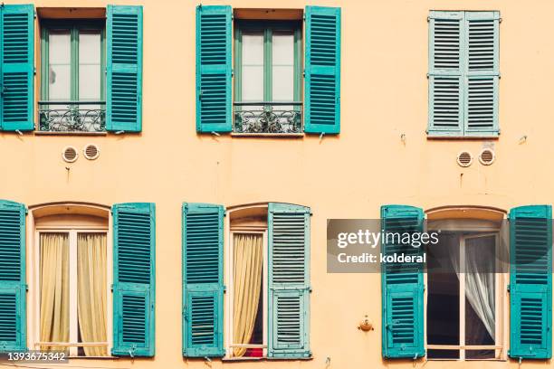 beautiful turquoise colored jalousie windows of renovated old apartment building with yellow walls in bright sunlight. full frame. old city of nice, france - provence france stock pictures, royalty-free photos & images