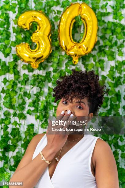 woman of black latin ethnicity celebrated and very happy at the thirty birthday party, golden balloons leaning on the wall, very surprised to turn years - 25 29 years stock-fotos und bilder