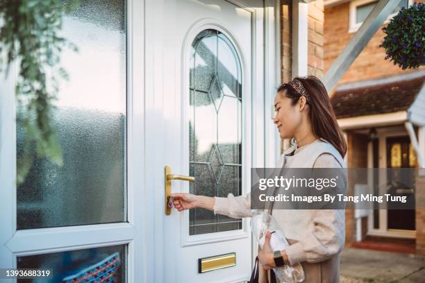 young cheerful asian woman unlocking the front door of her house - tür öffnen stock-fotos und bilder