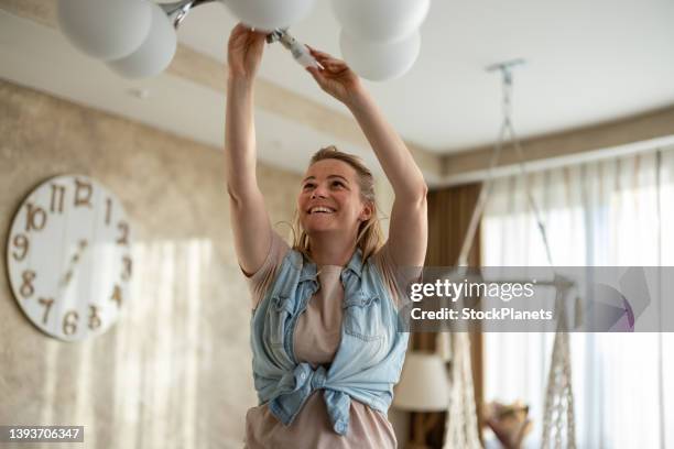 woman replaces an electric bulb in ceiling light fixture - gloeilamp stockfoto's en -beelden