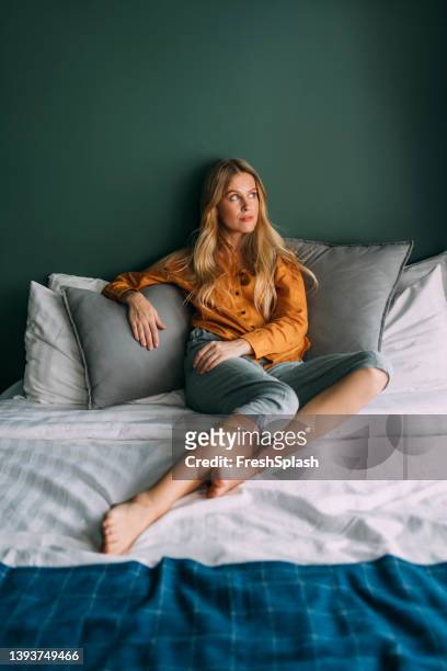 una bella donna bionda vestita casualmente sdraiata sul letto e distogliendo lo sguardo - donne bionde scalze foto e immagini stock