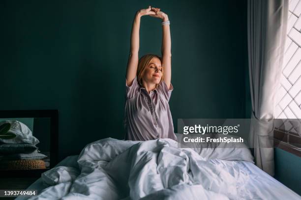 una bella donna bionda felice in pigiama che si sveglia e si allunga - wake up foto e immagini stock