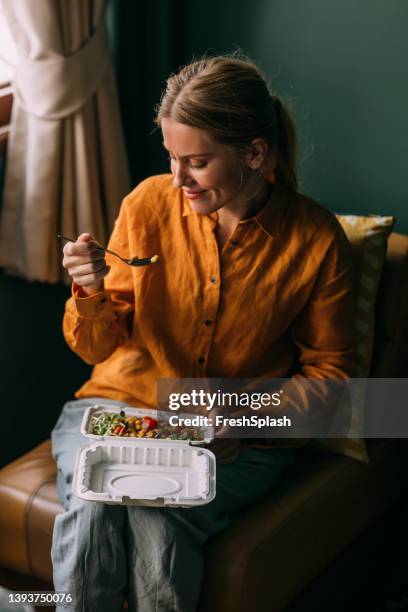 a beautiful blonde female sitting in her living room eating some healthy food - charming stock pictures, royalty-free photos & images
