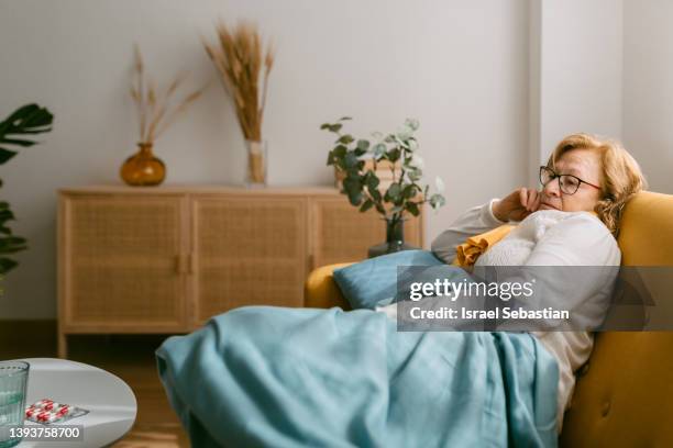 tired sick woman sitting on the sofa at home covered with a blanket. - ill home stockfoto's en -beelden