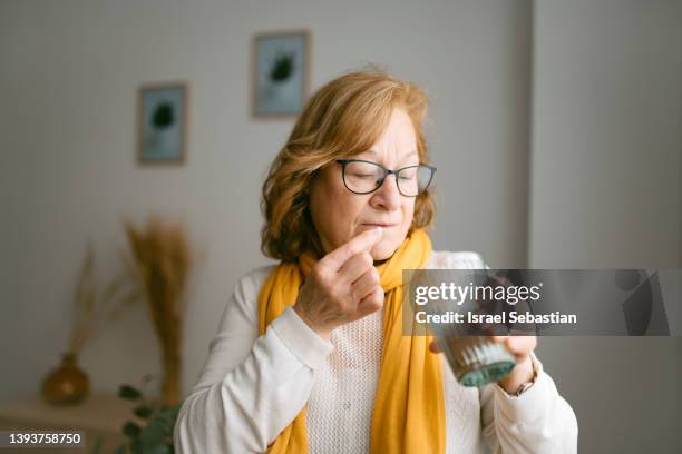 portrait of a mature woman taking pills and vitamins standing by the living room window. with copy space to the left. - taking pills stock pictures, royalty-free photos & images