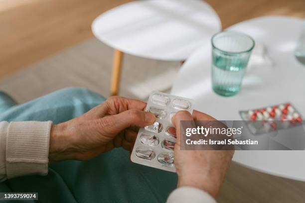 close up view of an unrecognizable woman taking a pill out of a blister pack - pijnstiller stockfoto's en -beelden