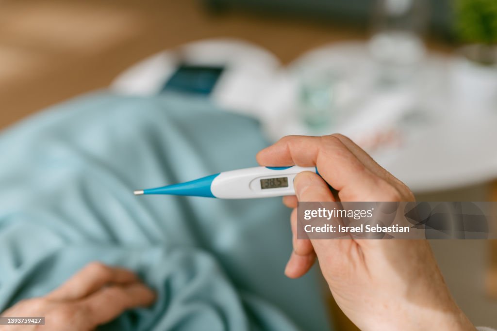 From above sick lady looking at thermometer while sitting on sofa.