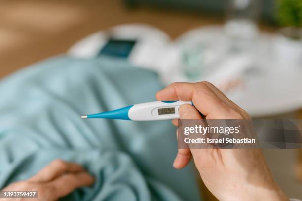 from above sick lady looking at thermometer while sitting on sofa. - influenza foto e immagini stock