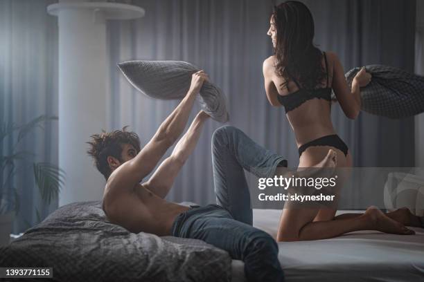 young happy couple having fun during a pillow fight on a bed. - pillow fight stock pictures, royalty-free photos & images