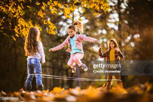 group of happy girls having fun while playing rubber band game in autumn day. - touwtje springen stockfoto's en -beelden