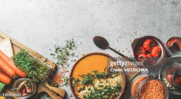 food background with homemade lentil soup with topping in bowl, vegetables, food staple and cooking utensils on grey kitchen table - sopa de curry - fotografias e filmes do acervo