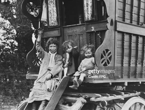 Roma children waving as they sit on the rear of their caravan on Epsom Downs in Surrey, England, circa 1935. These Roma children are among the many...