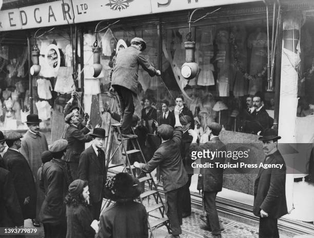 Small crowd gathers to watch as glaziers removing broken panes of glass from the Swan & Edgar department store after it had been targeted by the...