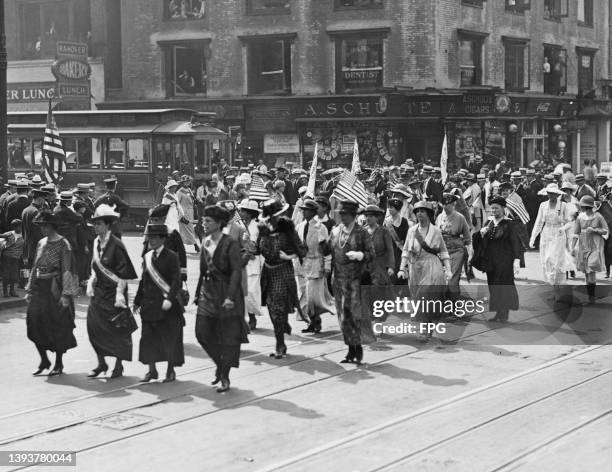Women's suffrage activists, some waving American flags, they pass along Seventh Avenue en route to the Waldorf in a victory parade in New York City,...