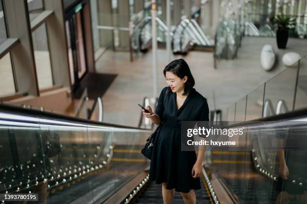 young businesswoman using smartphone while riding on escalator - business travel asian stock pictures, royalty-free photos & images