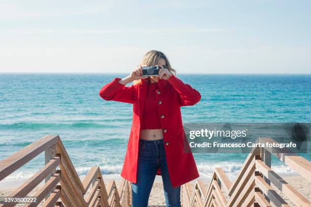 woman taking a photo with a film camera - red coat foto e immagini stock