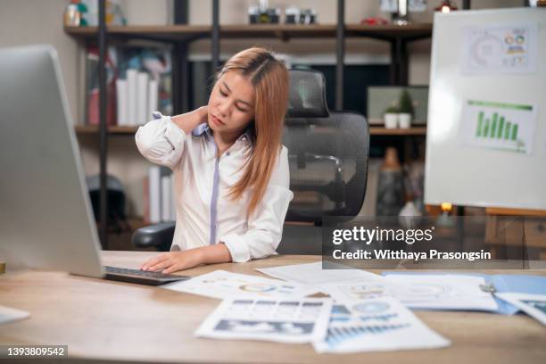 office syndrome concept. young asian businesswoman feeling pain in neck after working on computer laptop - stretching at desk stock pictures, royalty-free photos & images