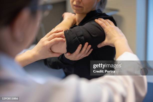 close-up of a doctor examining arm of woman patient in clinic - shoulder stock pictures, royalty-free photos & images