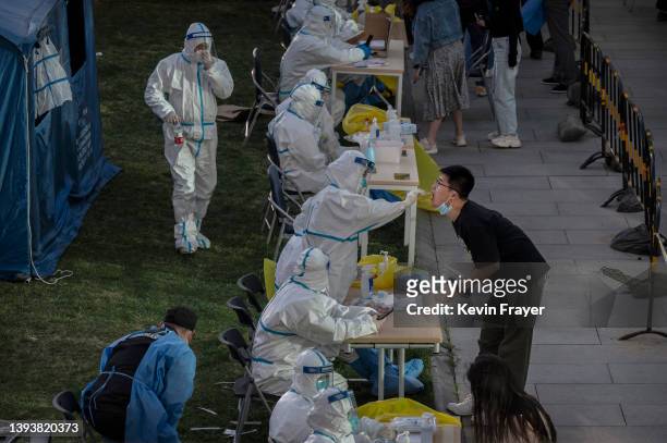 Health worker wears a protective suit as an employee from a local company is given a nucleic acid test to detect COVID-19 at a makeshift testing site...