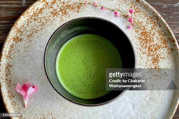green tea - matcha, in a dark bowl on the vintage white plate decorated with pink flower. table top view. - heritage round one stock-fotos und bilder