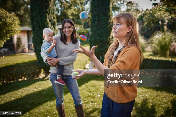 woman juggling with balls in garden watched byther with child - drei erwachsene stock-fotos und bilder