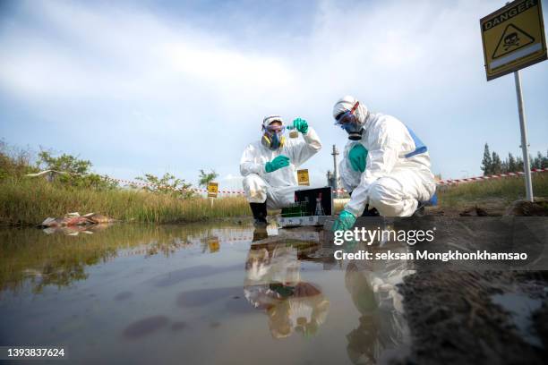 male scientist reading ph value or examining toxic water from a water sample. he working outdoors and wearing protective workware coveralls. - controle de qualidade imagens e fotografias de stock