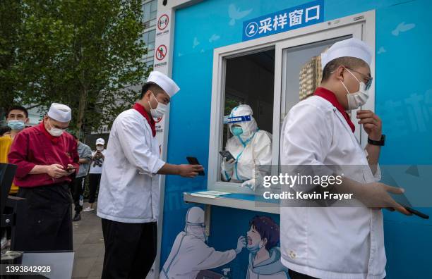 Health worker wears protective clothing as restaurant workers scan to register for a nucleic acid test to detect COVID-19 at a makeshift testing site...