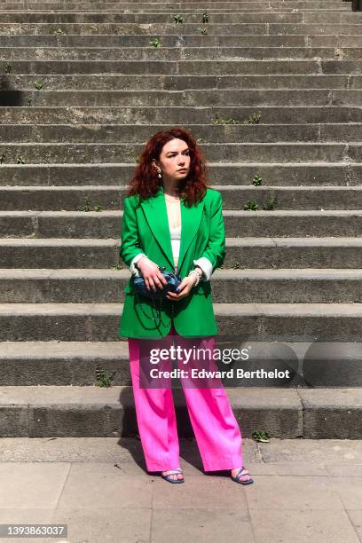 Nastasia Iavorscaia wears a gold and pearl pendant earrings, a gold necklace, a white V-neck / cropped t-shirt, a green oversized long blazer jacket...