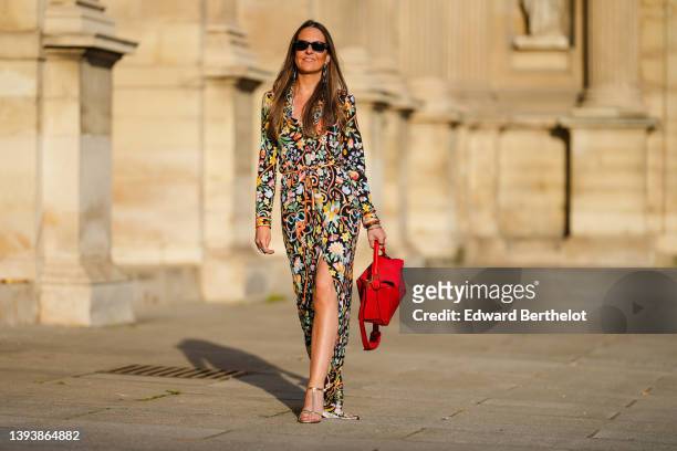 Alba Garavito Torre wears black sunglasses from Ray Ban, a black with multicolored print pattern V-neck / long sleeves / belted / flowing dress from...