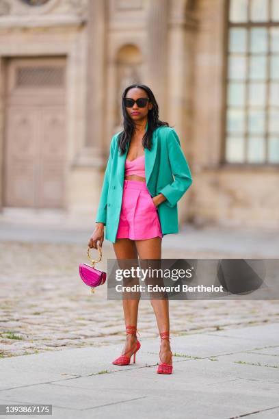 Emilie Joseph wears black sunglasses, rhinestone earrings, a turquoise blue oversized blazer jacket, a strappy / ribbed V-neck cropped tank-top from...