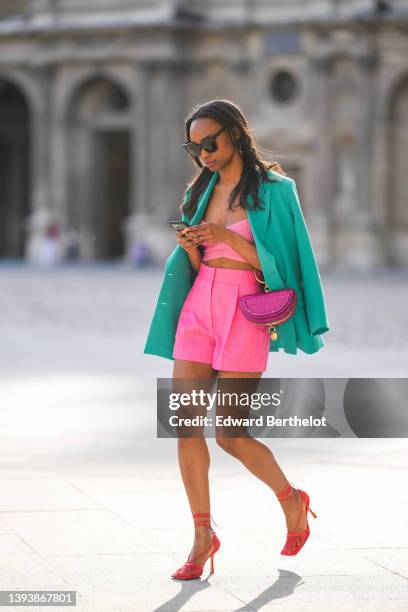 Emilie Joseph wears black sunglasses, rhinestone earrings, a turquoise blue oversized blazer jacket, a strappy / ribbed V-neck cropped tank-top from...