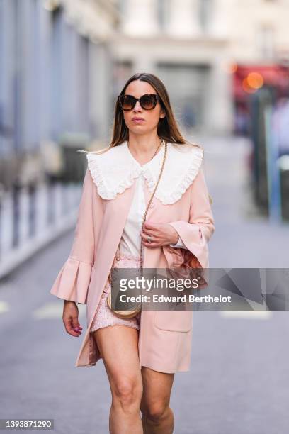 Maria Rosaria Rizzo wears brown sunglasses, a white with lace pattern oversized blouse / shirt from La petite Étoile, a beige shiny leather circle...