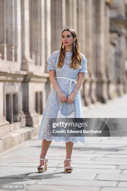 Maria Rosaria Rizzo wears oversized gray blue and white pendant pattern earrings from Rosa Ladisa, a pale blue cut-out lace pattern midi dress with...