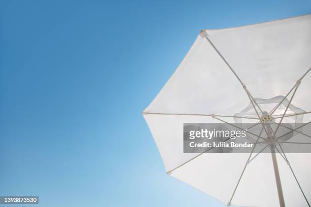 white sun umbrella over the blue sky - sombrilla fotografías e imágenes de stock