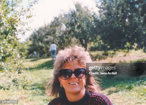vintage 1980s hairstyle, stylish 1990s hair, happy woman wearing sunglasses outdoors apple picking - 80s hair bildbanksfoton och bilder